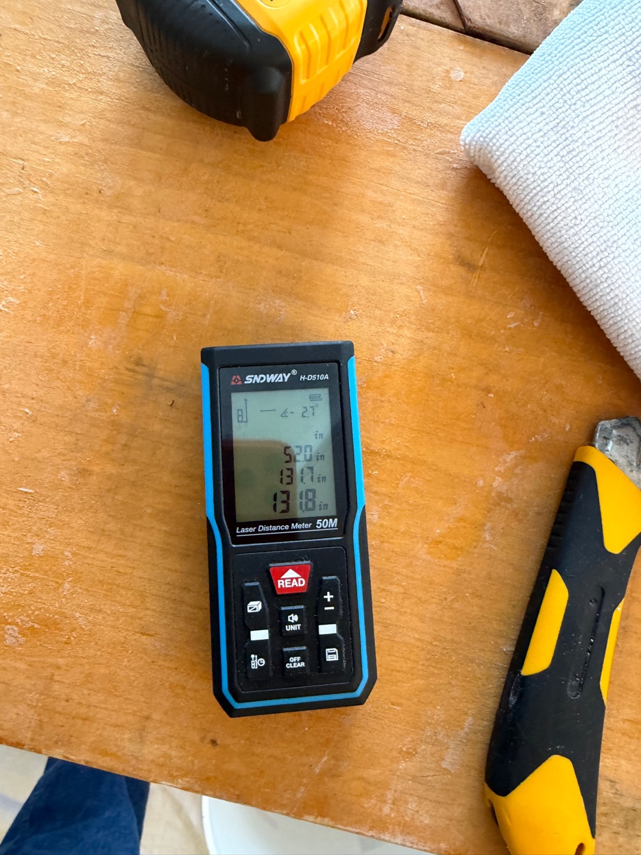 Laser distance meter and hand tools used to measure a wall before a wallpaper installation.