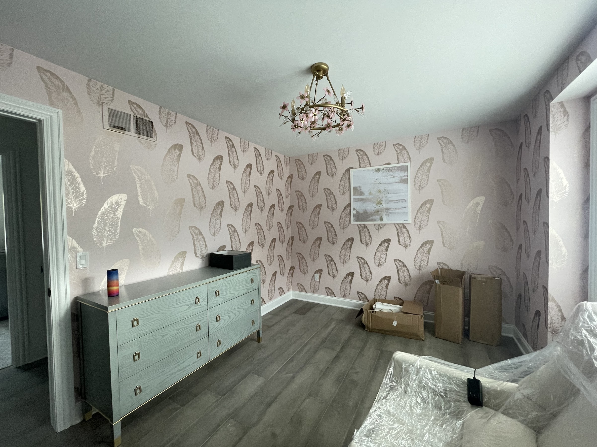 Finished bedroom in a soft taupe feather wallpaper — a non-woven, paste-the-wall paper hung with tight seams, styled with a green dresser and floral chandelier. Installed by Bernau Designs.
