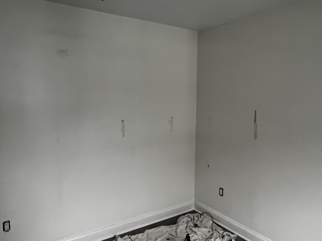 Bedroom wall stripped back to bare, primed drywall after peel-and-stick wallpaper was removed and the surface reset for a new installation.