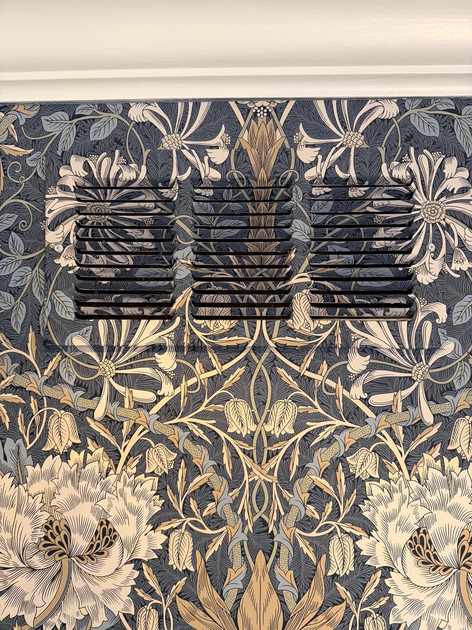 HVAC return vent precisely cut and matched into Morris & Co. Honeysuckle & Tulip wallpaper so the pattern carries across it.