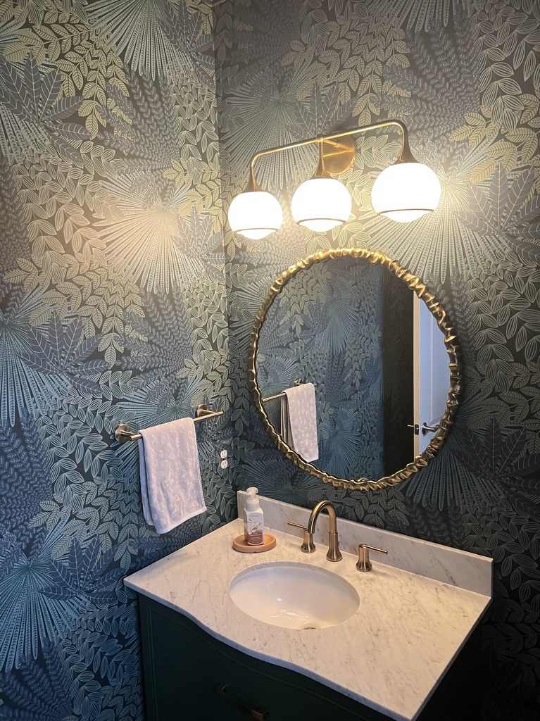 Bor&aring;stapeter Velvet Leaves wallpaper in Spruce and Blue on a powder room wall, with a round brass mirror and three globe sconces. Installed by Bernau Designs in Metro Detroit, Michigan.