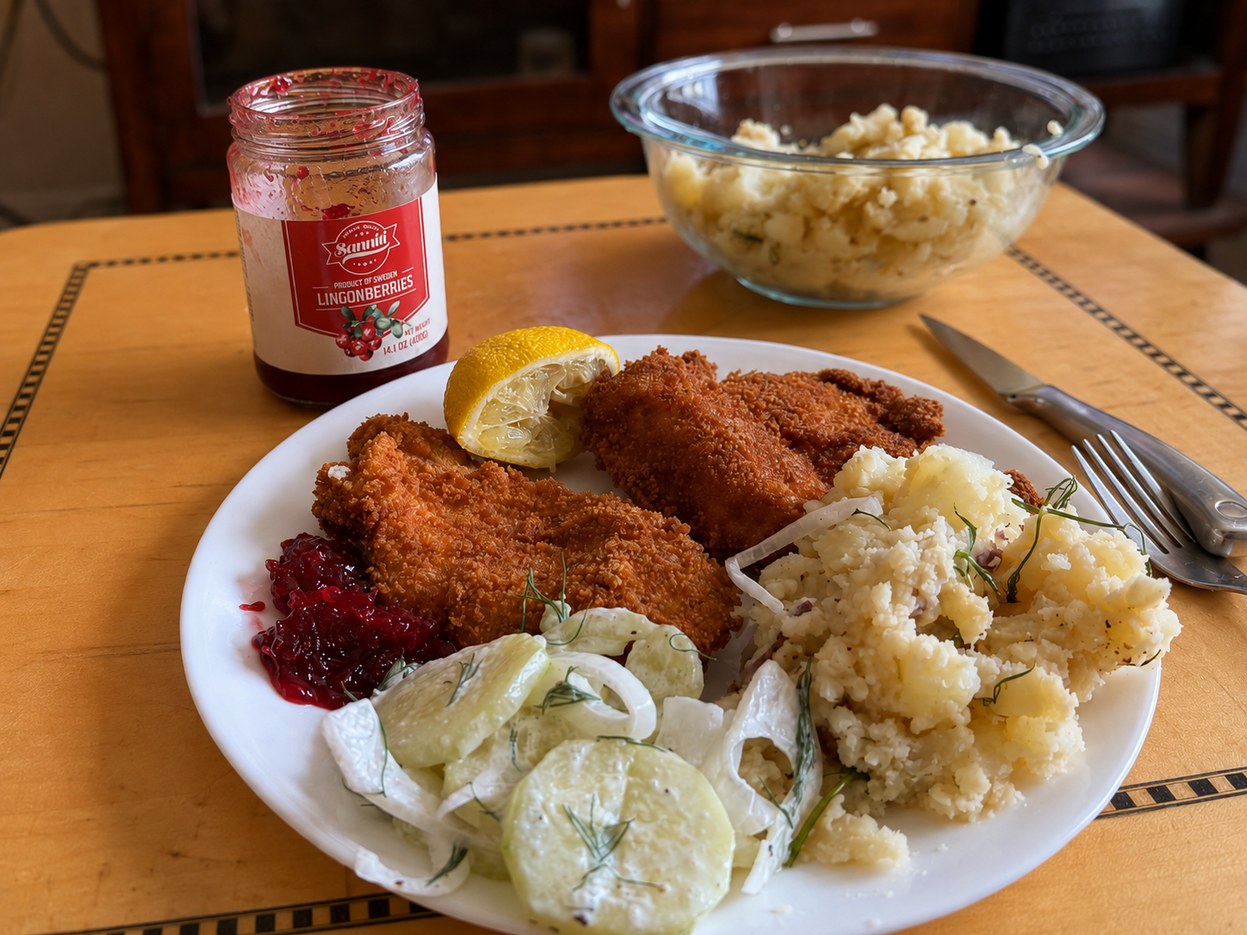 Homemade breaded schnitzel with potato salad, cucumber salad and lingonberry preserves, beside a jar of lingonberries labelled Product of Sweden.