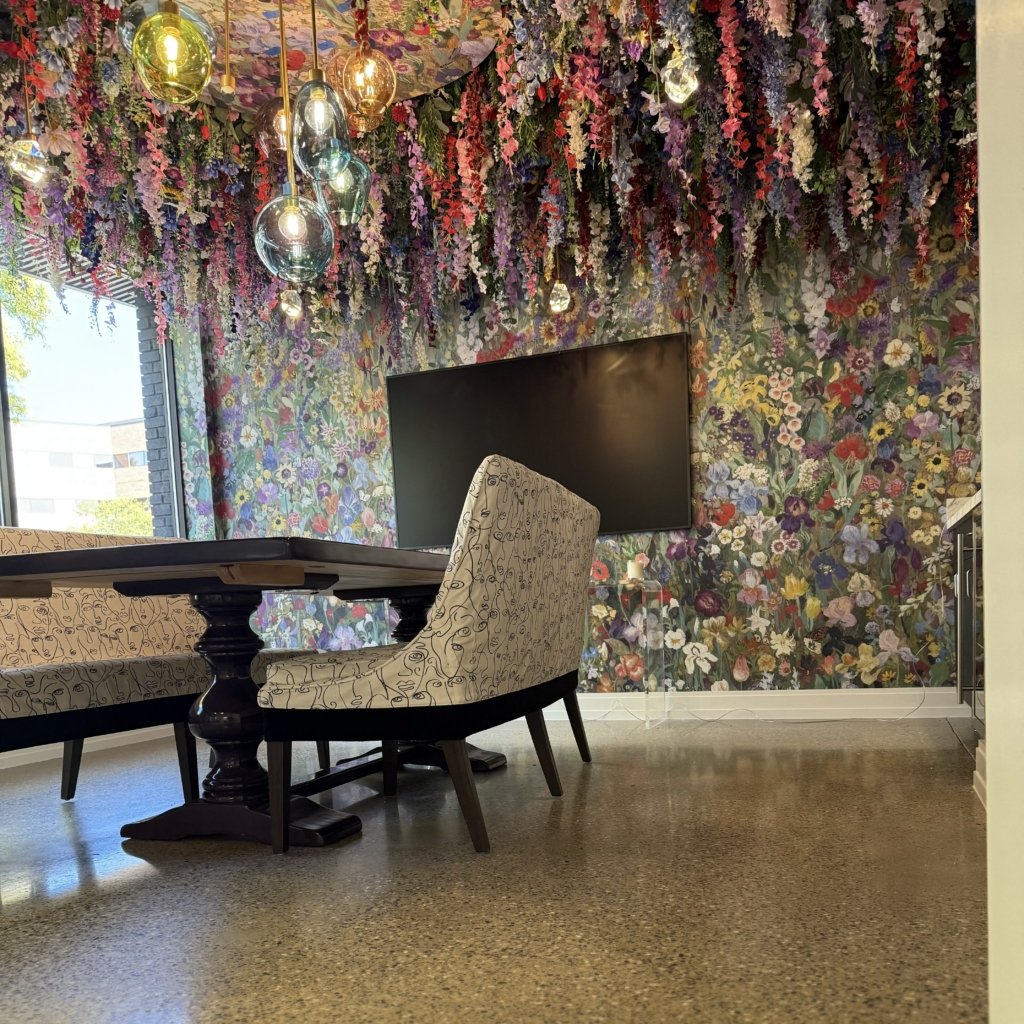 A room at GlamJail in Birmingham, Michigan with dense floral wallpaper covering the walls and continuing across the ceiling, hung with glass pendant lights.