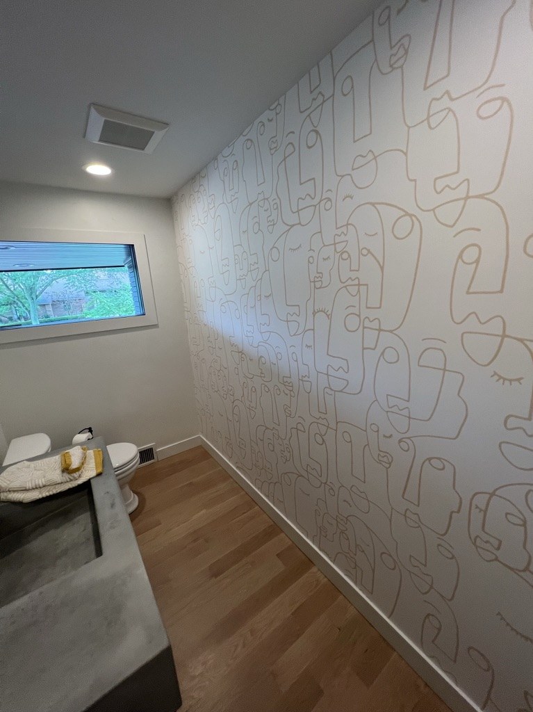 Continuous line-drawing face mural in soft grey on a pale ground, installed in a Michigan powder room by Bernau Designs.