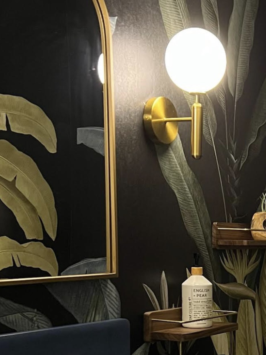 Bare globe sconce mounted close to a dark Hovia tropical mural, with the wall reading flat and continuous under harsh direct light.