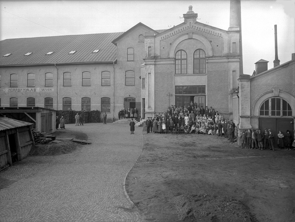 The assembled workforce of Norrby Nya A.B. standing in the mill yard in Bor&aring;s, Sweden in 1919, in front of a brick building dated 1876.