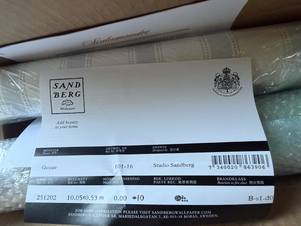 A Sandberg Wallpaper roll label showing pattern Gustav, article number 101-16, roll size 10.05 by 0.53 metres, fire class B-s1,d0, a Swedish royal warrant crest, and the address Mariedalsgatan 7, Bor&aring;s, Sweden.