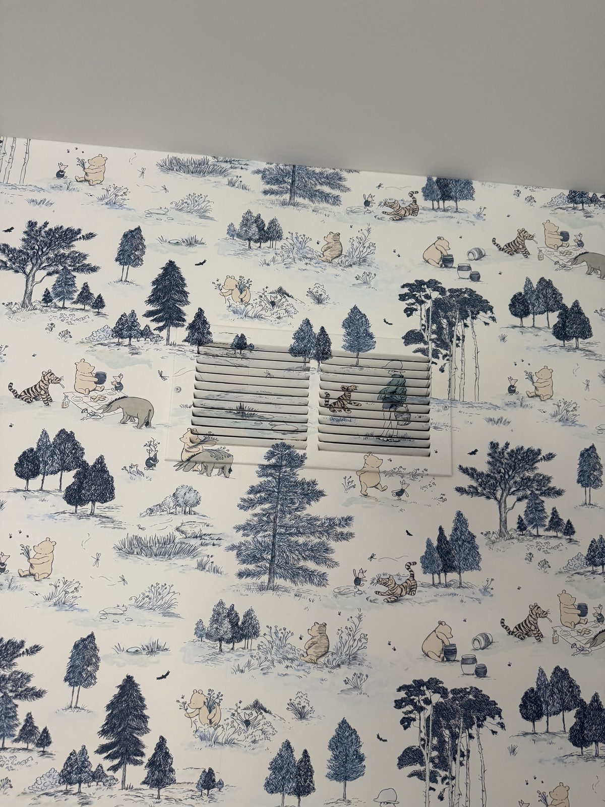 Wallpapered return-air vent with the forest scene continuing across the grille in a Winnie the Pooh nursery.
