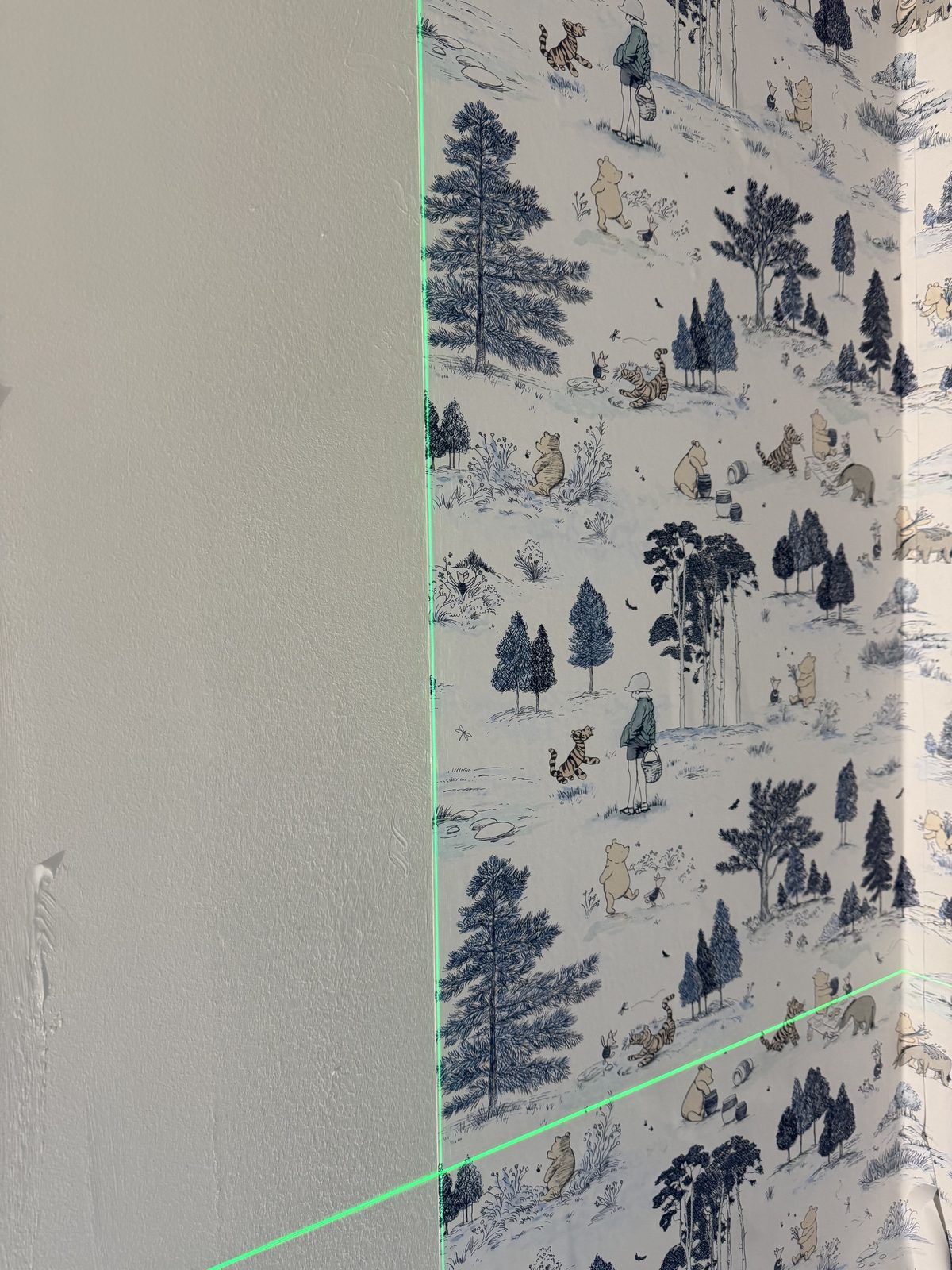 Cross-line laser establishing vertical and horizontal reference for wallpaper layout in a Plymouth nursery installation.