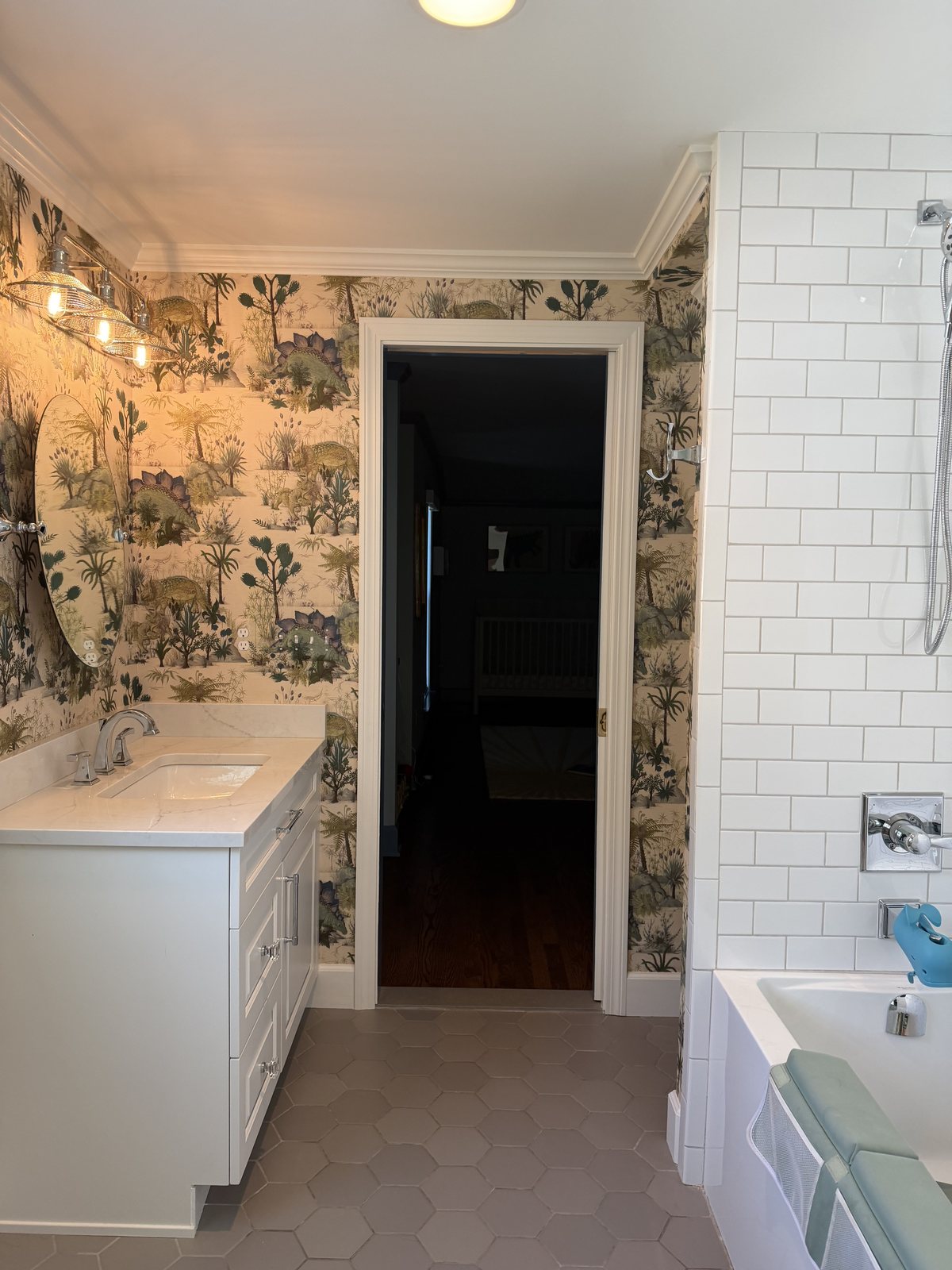 Dinosauria Ecru wallpaper on the dry walls of a children's bathroom, with white subway tile at the tub and a gray hexagon tile floor.