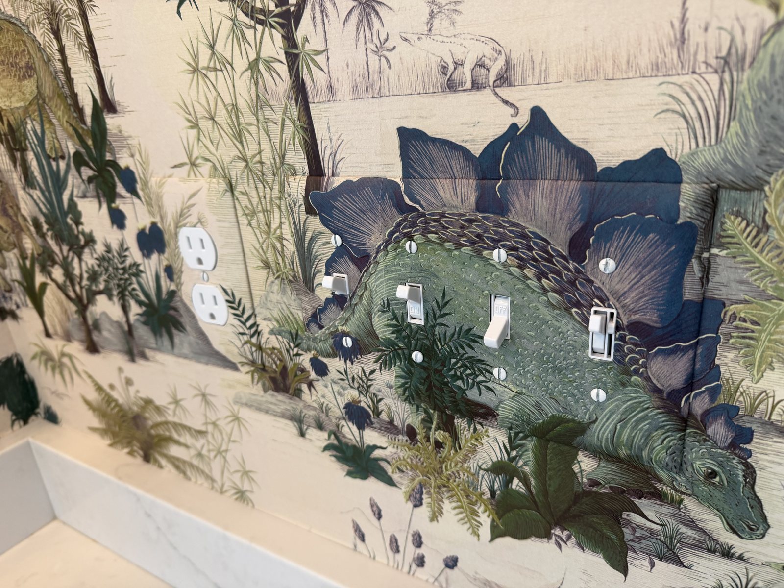House of Hackney Dinosauria Ecru wallpaper installed around switches in a children's bathroom.