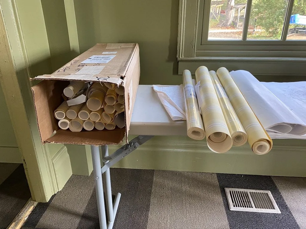 Rolls of Kensington Stripe wallcovering staged on a folding table in a green-painted room at the Niles-Barnard House.