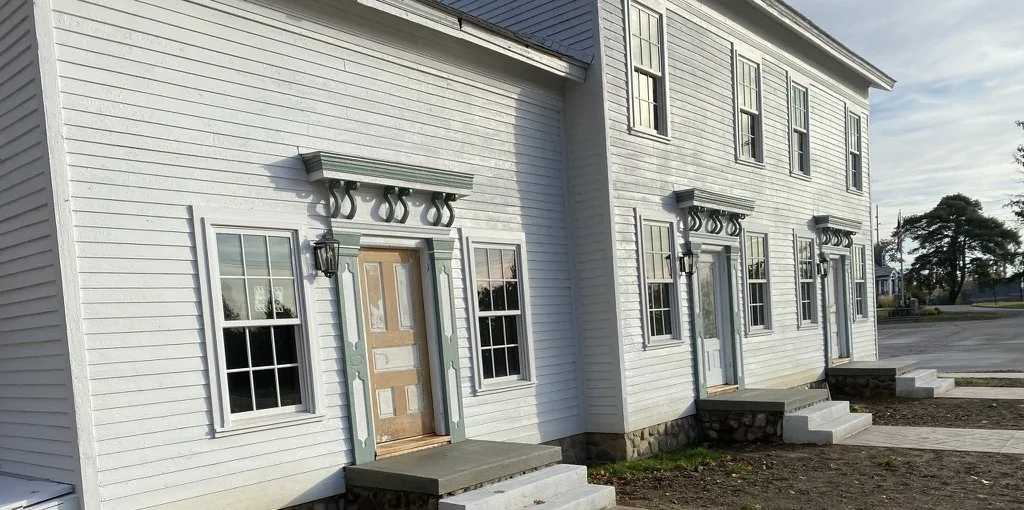 Exterior of the Niles-Barnard House at Troy Historic Village in Troy, Michigan, white clapboard with sage green trim and three bracketed front door hoods.